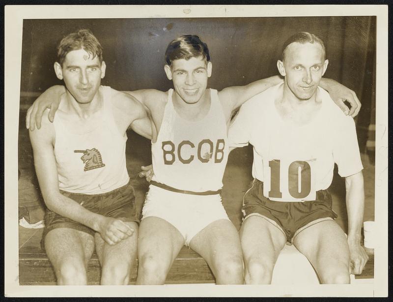 Three runners seated on a bench with arms around each other. The man in the center wears a singlet lettered BCOB.