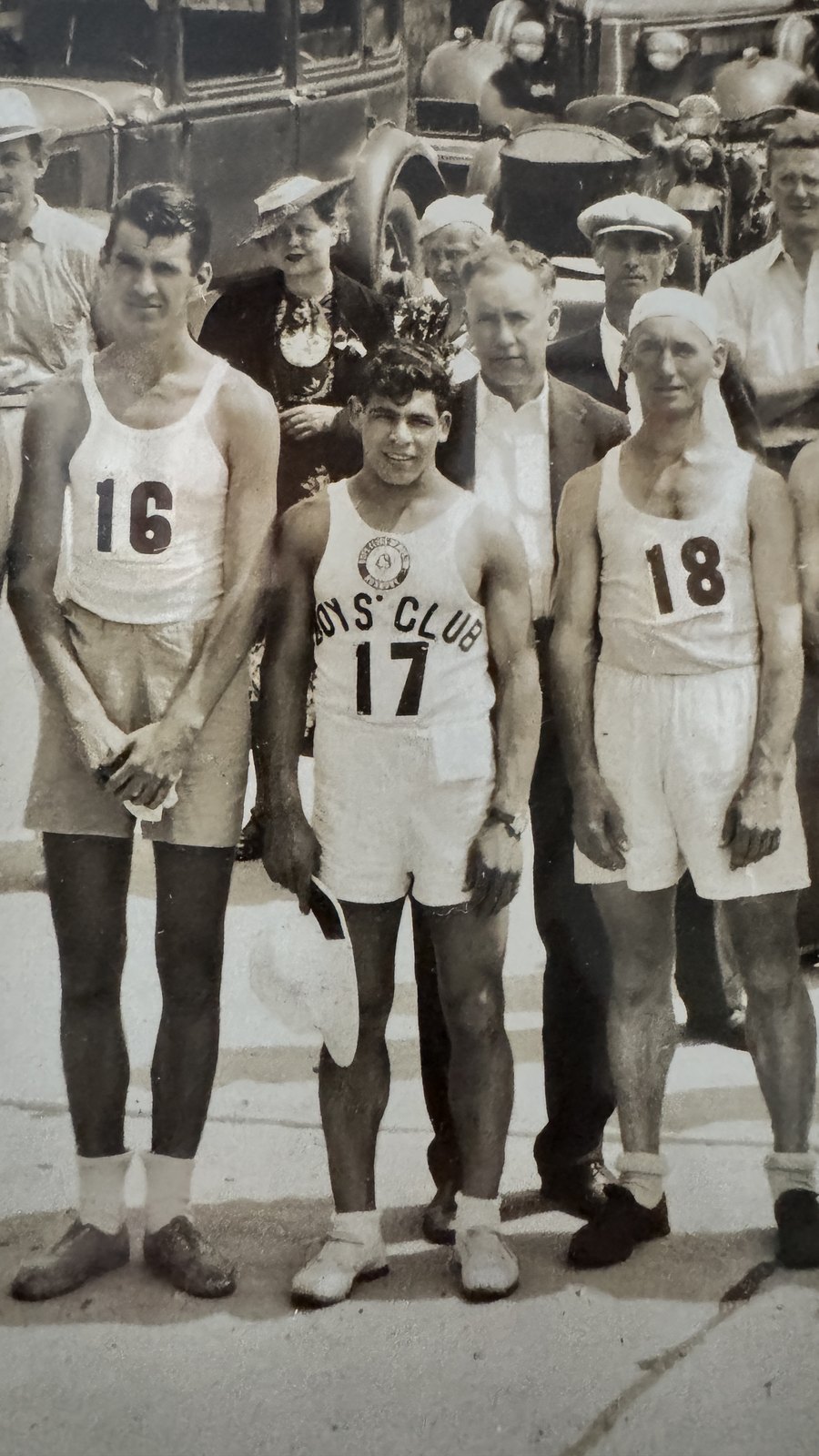 Magnified detail from the panorama showing a dark haired young runner in a Boys Club singlet numbered 17, standing between runners numbered 16 and 18.