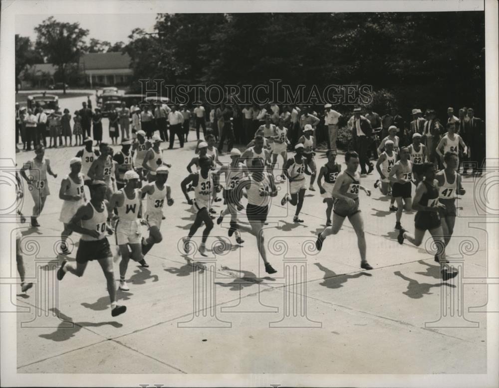 Press photograph of the start of a marathon, dozens of runners moving away down a paved road past a crowd of spectators.