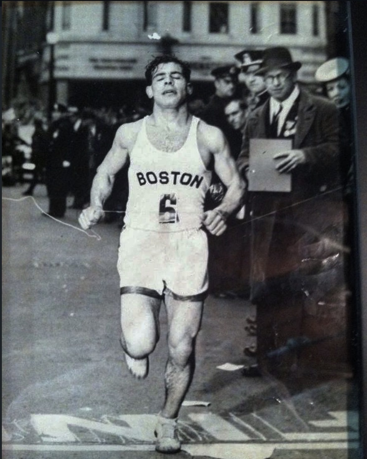Paul Donato finishing the Boston Marathon, wearing a white singlet lettered BOSTON with race number 6, police and officials watching from the kerb.